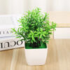 Mini artificial green plant in a modern white pot sitting on a wooden desk next to books.