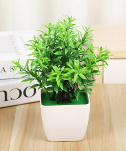 Mini artificial green plant in a modern white pot sitting on a wooden desk next to books.