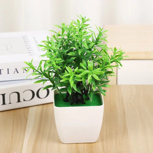 Mini artificial green plant in a modern white pot sitting on a wooden desk next to books.